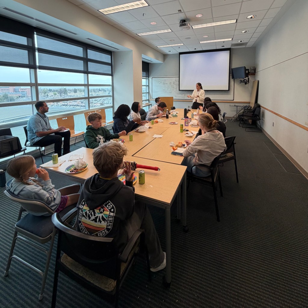 Betsy presenting to the Witowski Lab team, her three kids in the foreground